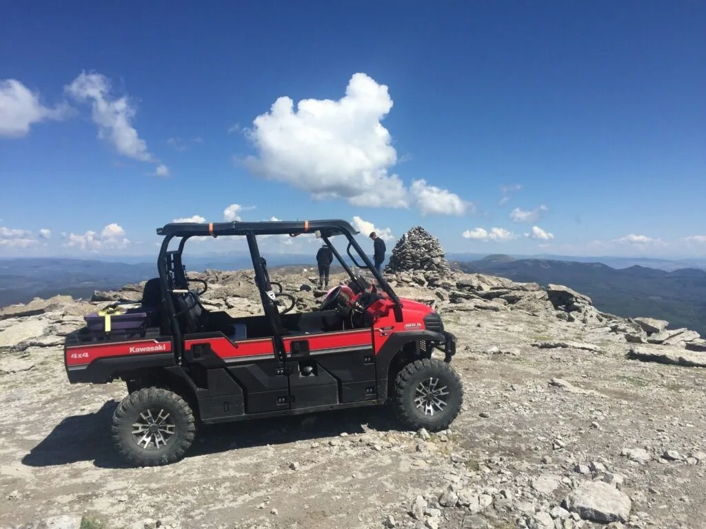 A red six-seat Kawasaki side-by-side parked on a rocky summit